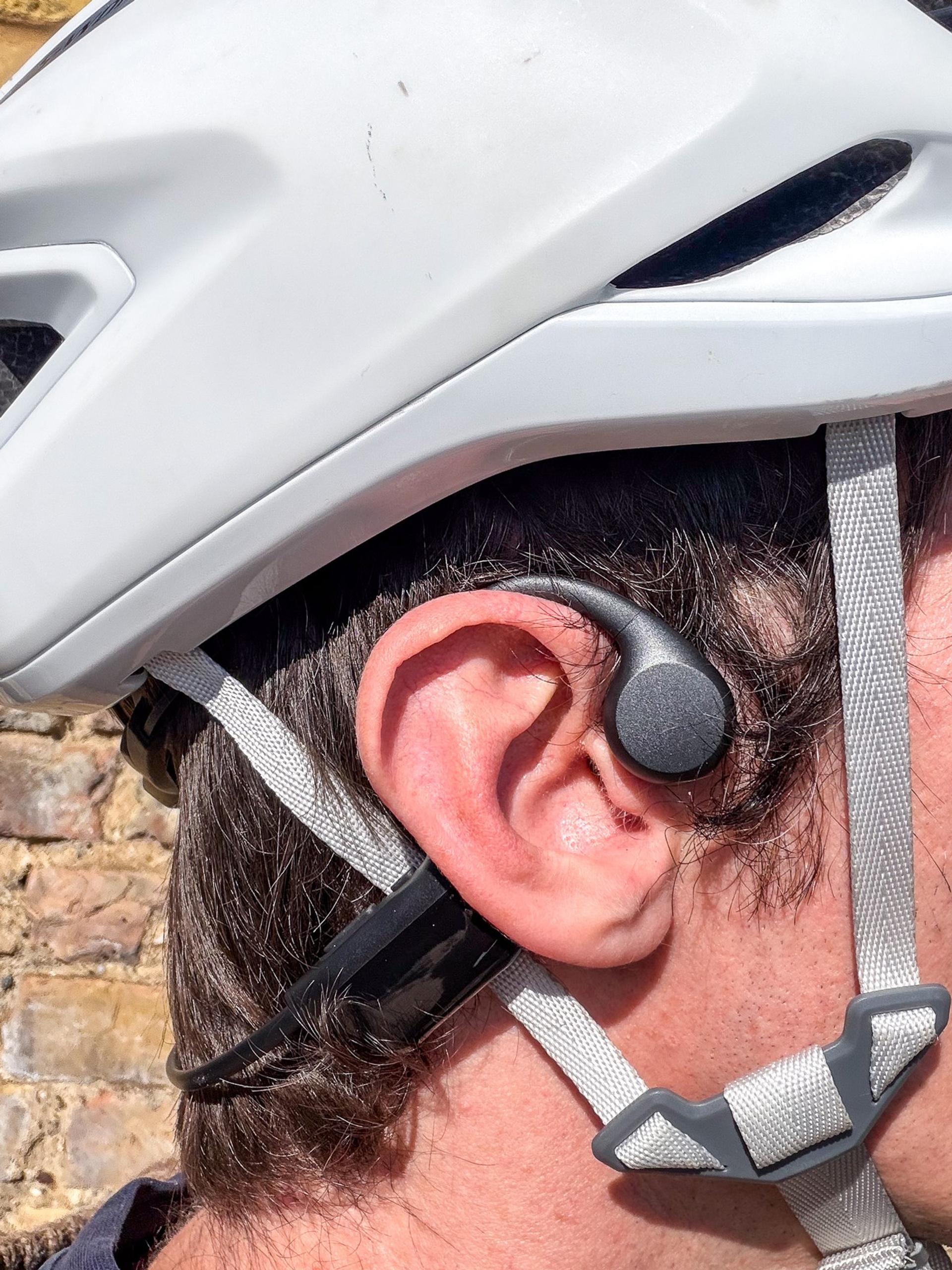 Close-up of a person wearing Zovimax bone-conduction headphones, with the earpiece resting in front of the ear.