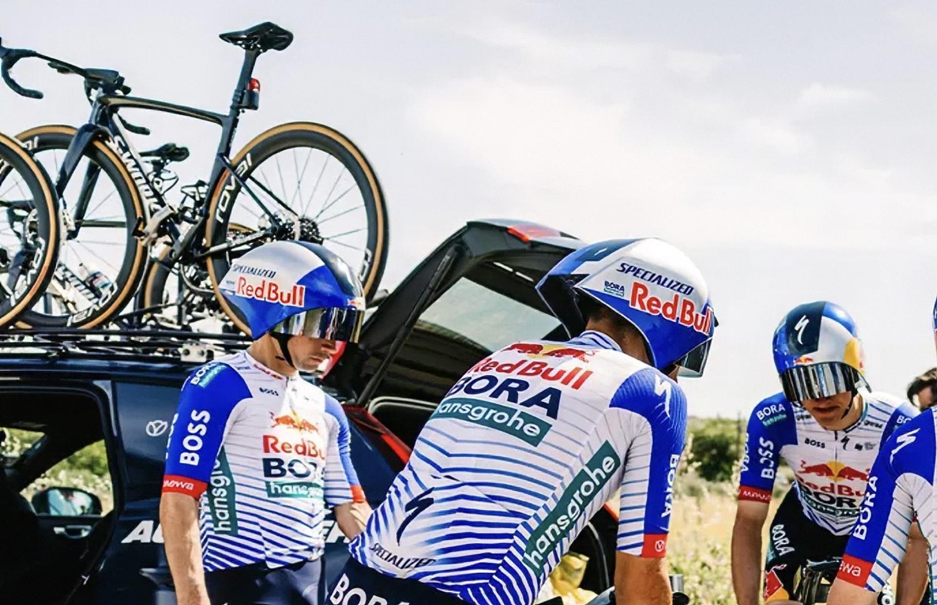 Red Bull cycling team members celebrate near bikes after a race, wearing team jerseys and helmets.
