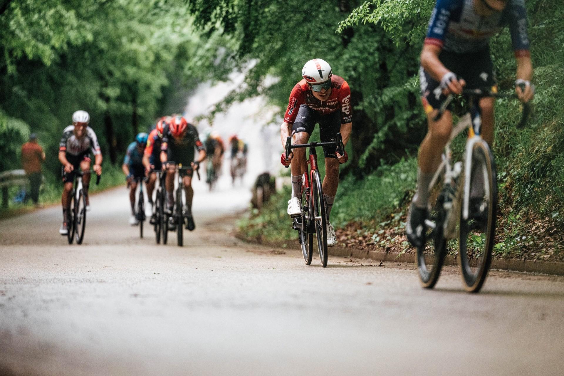 Lennert Van Eetvelt rides at the front of a group of cyclists on a tree-lined road.