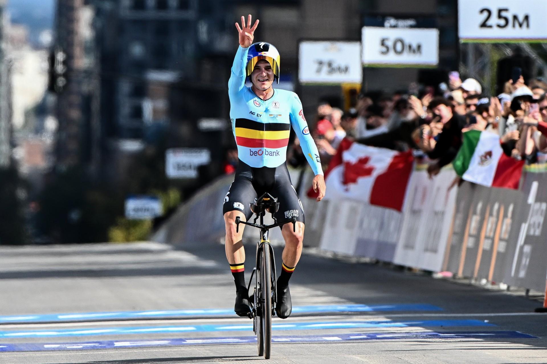 Remco Evenepoel raises a hand while crossing the finish line as crowds cheer at the World Championships.