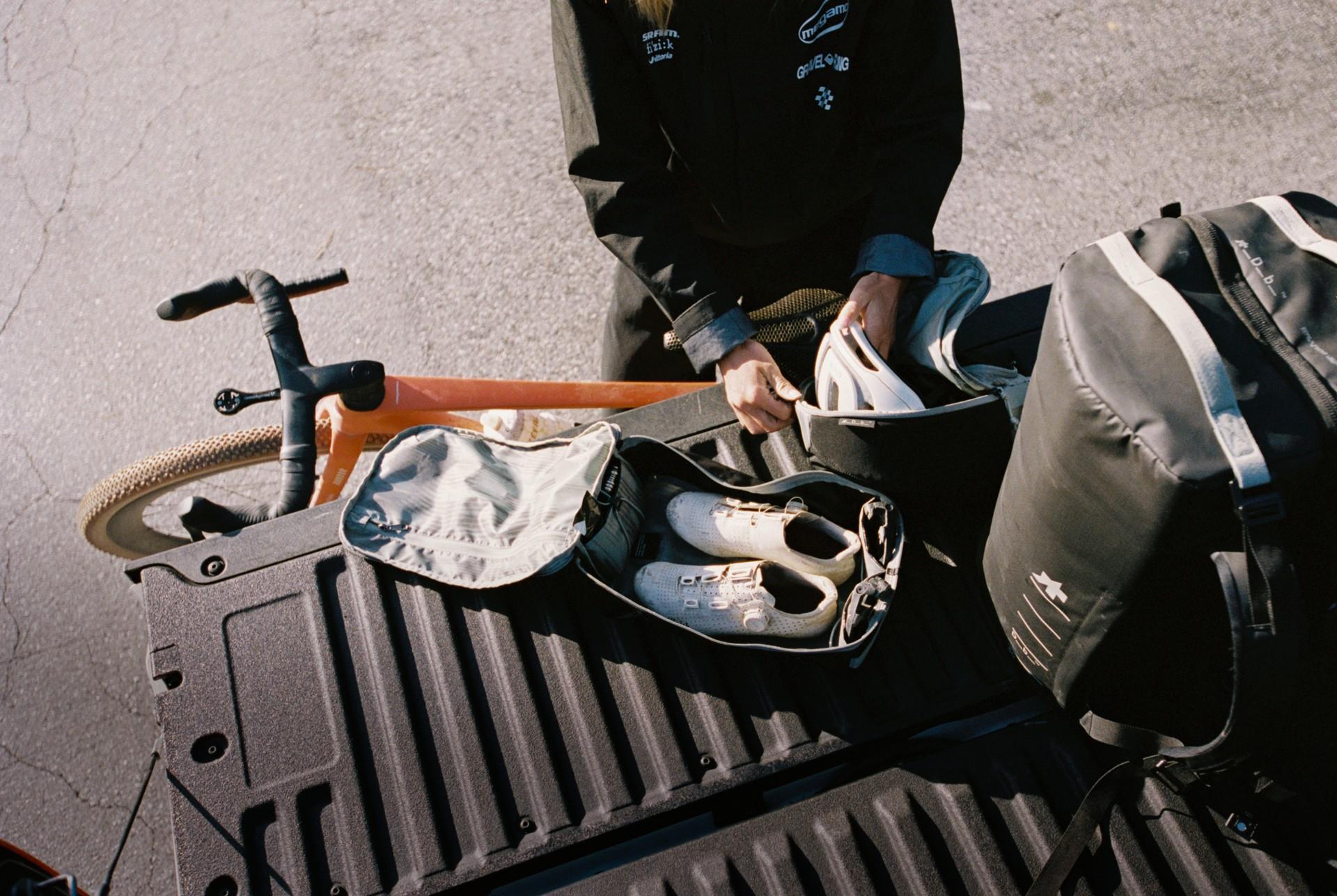 Cyclist seated on a bike at a track event, adjusting gear inside a black case