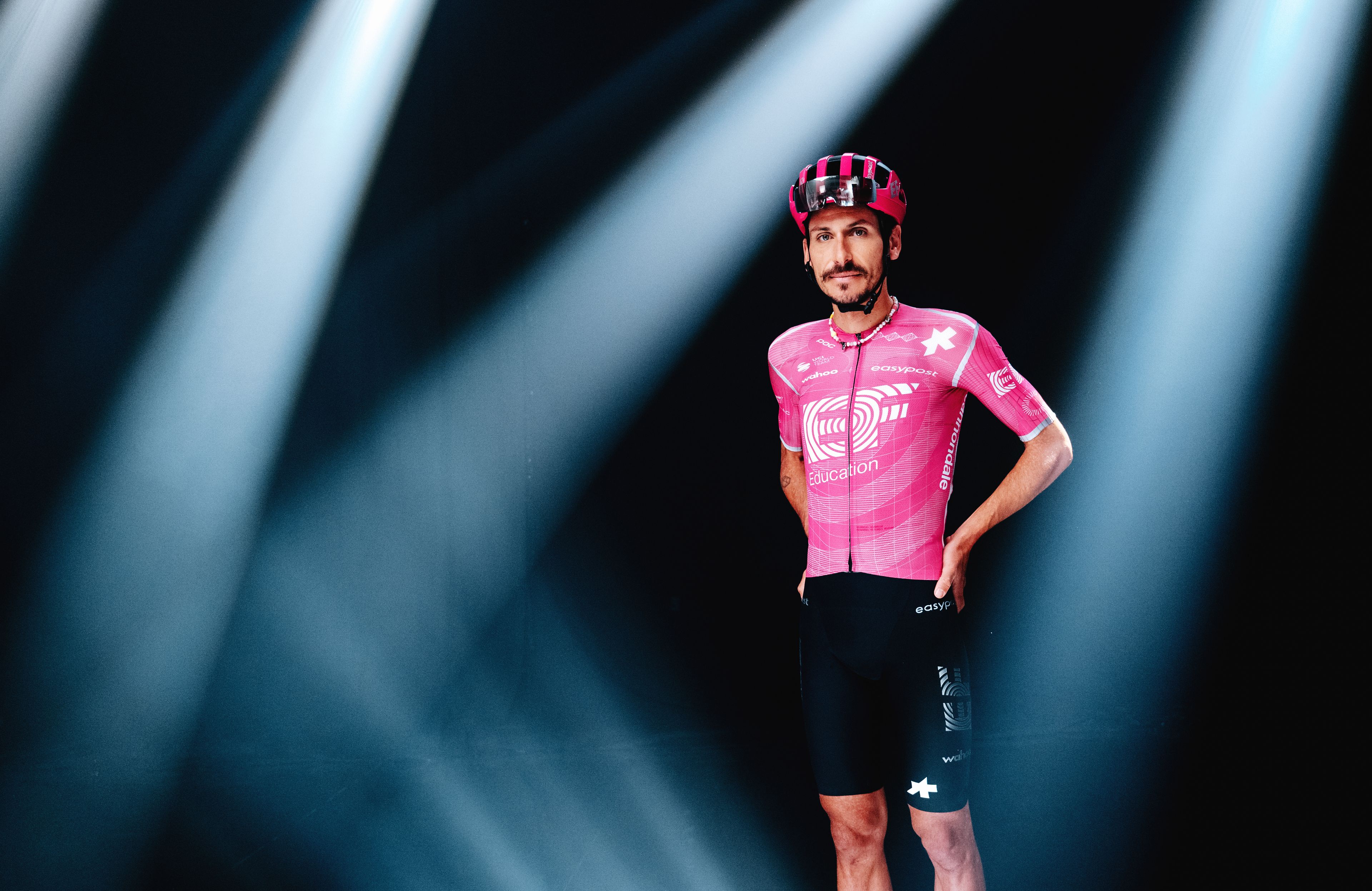 Lachlan Morton appears in the campaign wearing the team’s ASSOS kit, presented in a dramatic studio setup with spotlight lighting.