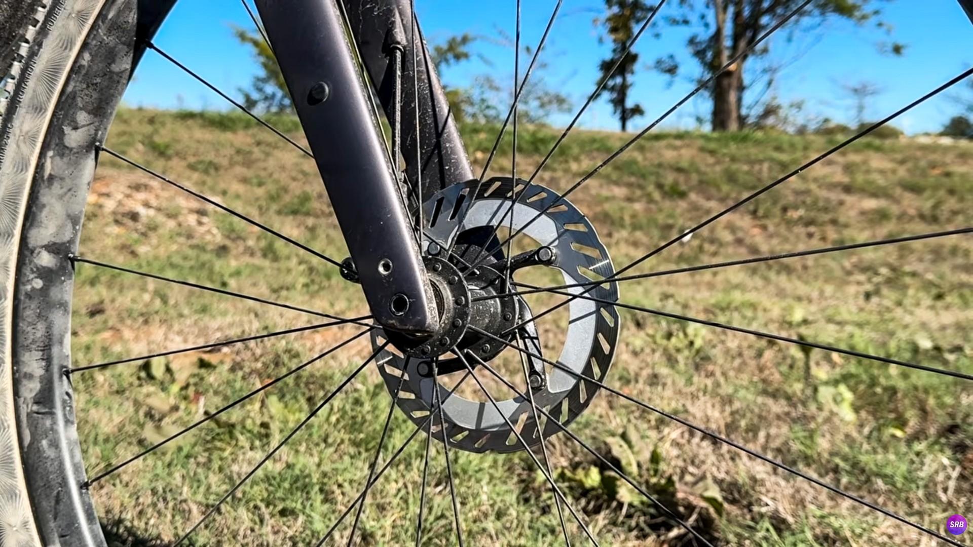 Close-up of a bicycle’s front wheel, disc brake rotor and fork outdoors