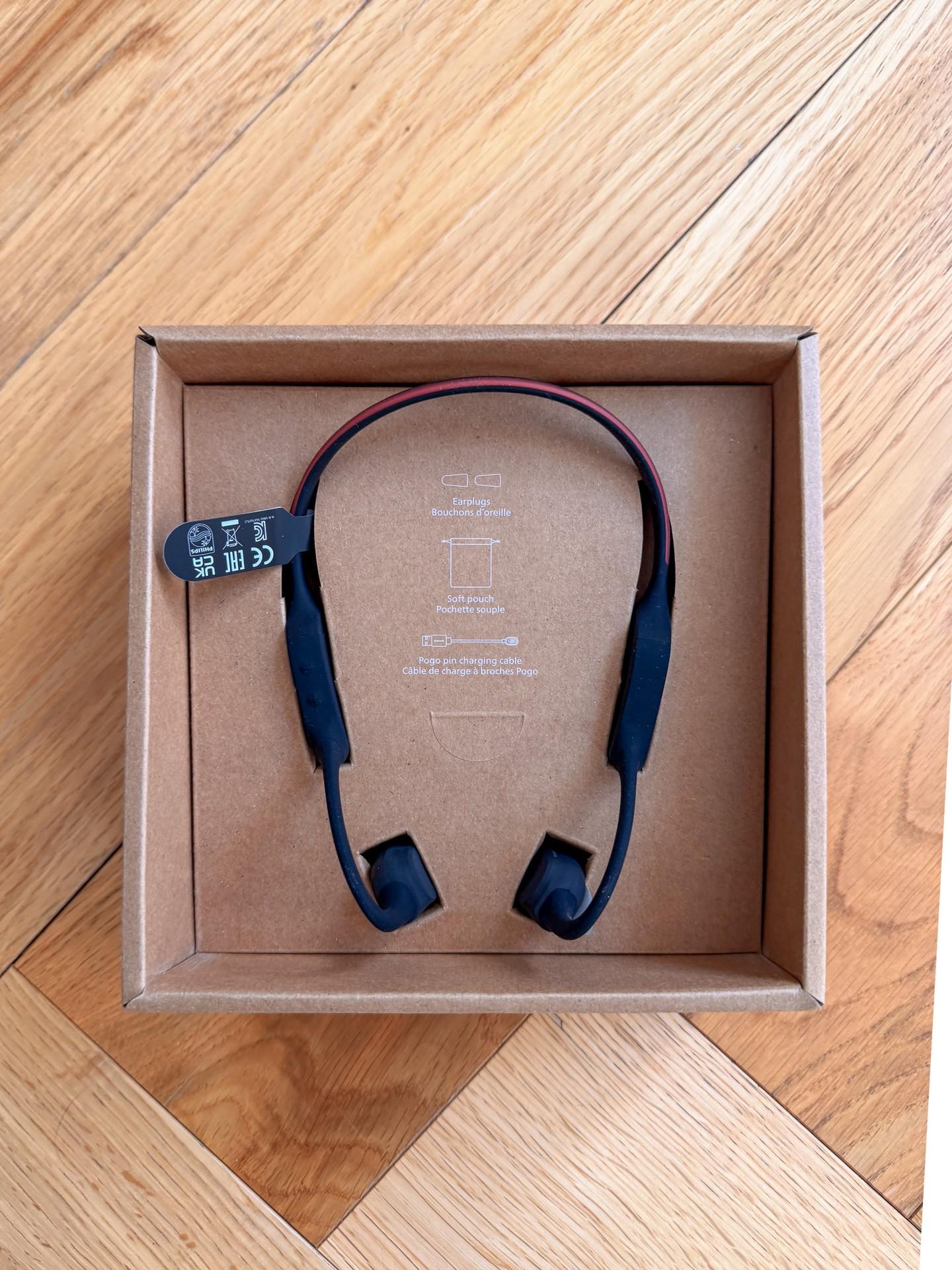 Philips open-ear sports headphones with a blue neckband and red rear LED strip displayed in an open box