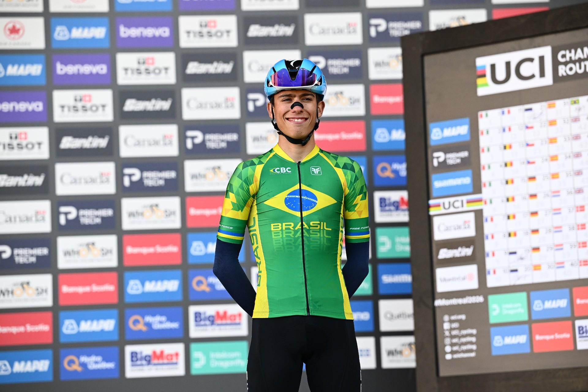 Henrique Bravo in a green-and-blue cycling kit stands in front of a sponsor-logo backdrop.