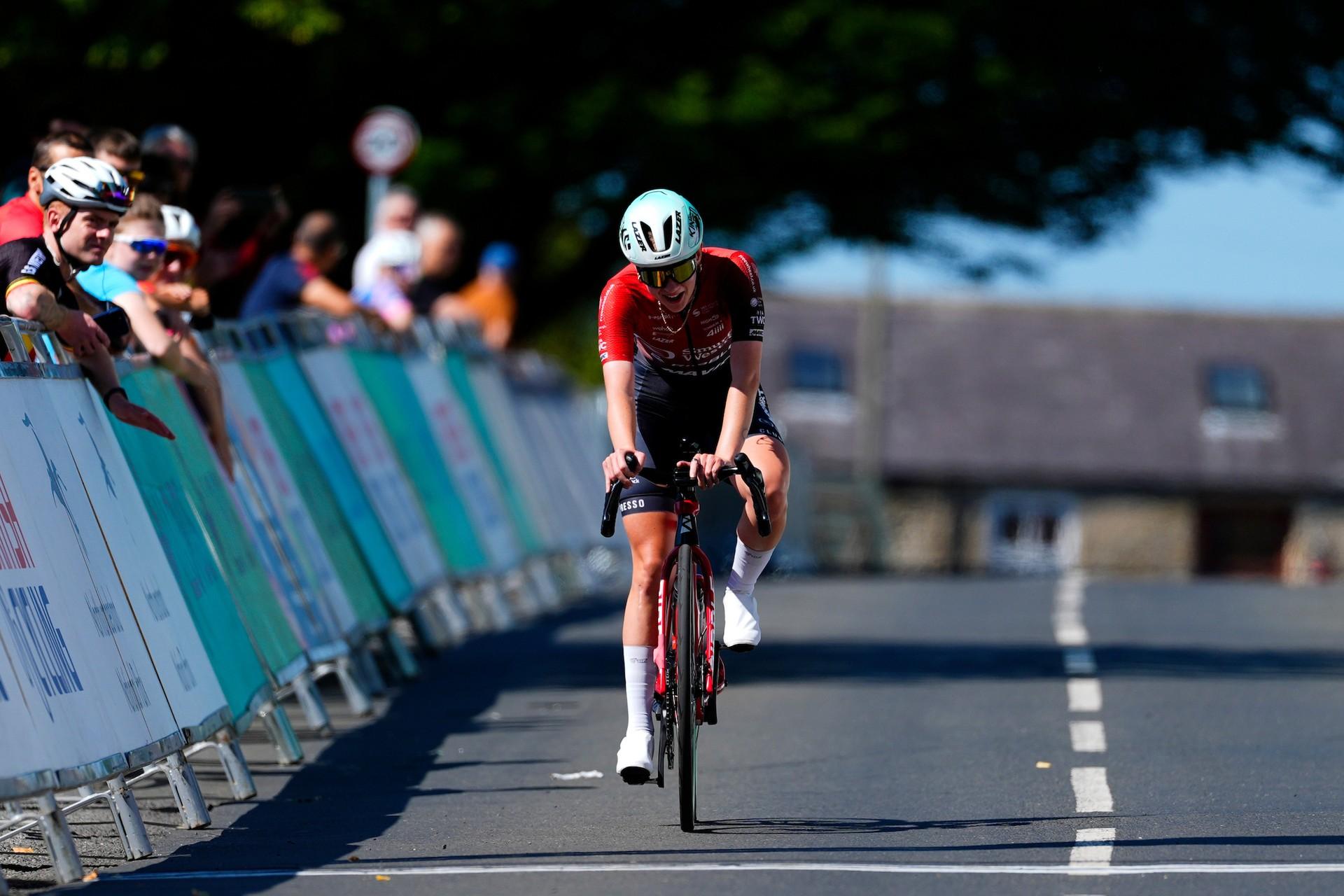Grace Reynolds rides her bike along a race course, with spectators watching from behind barriers.