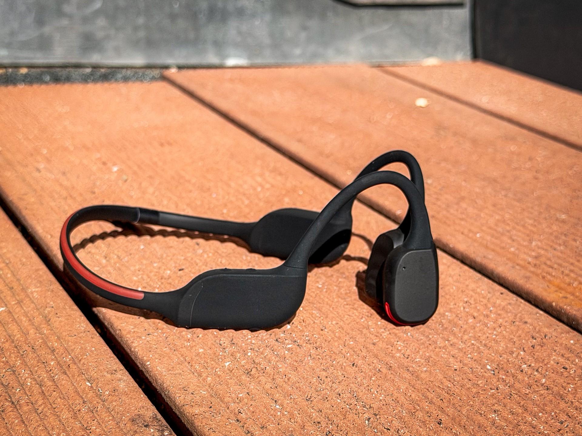 Philips TAA7607BK open-ear sports headphones lying on a wooden surface, with their wraparound band and rear LED visible.