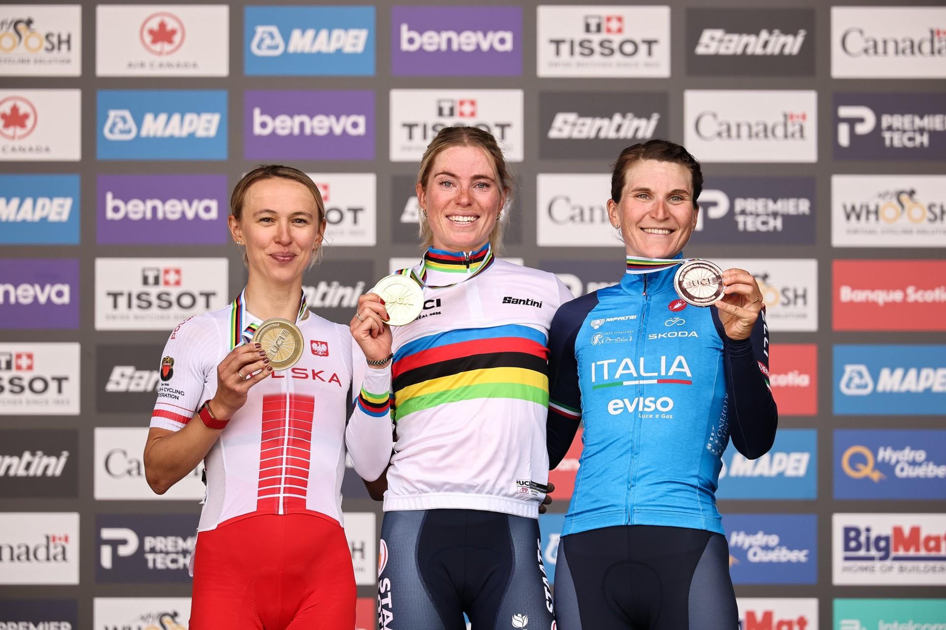 Demi Vollering, Kasia Niewiadoma-Phinney and Elisa Longo Borghini pose in cycling jerseys before a sponsor backdrop.