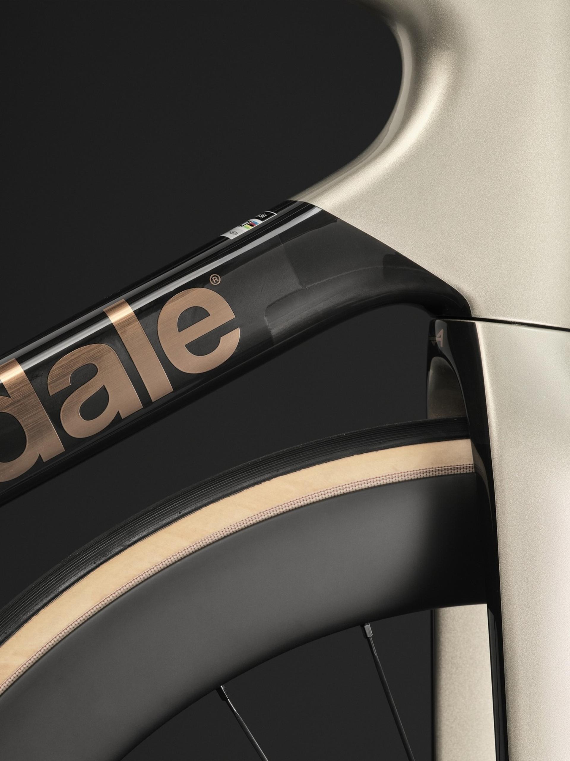 Close-up of a Cannondale road bike frame in champagne gold and black with copper branding and tan-wall tires.