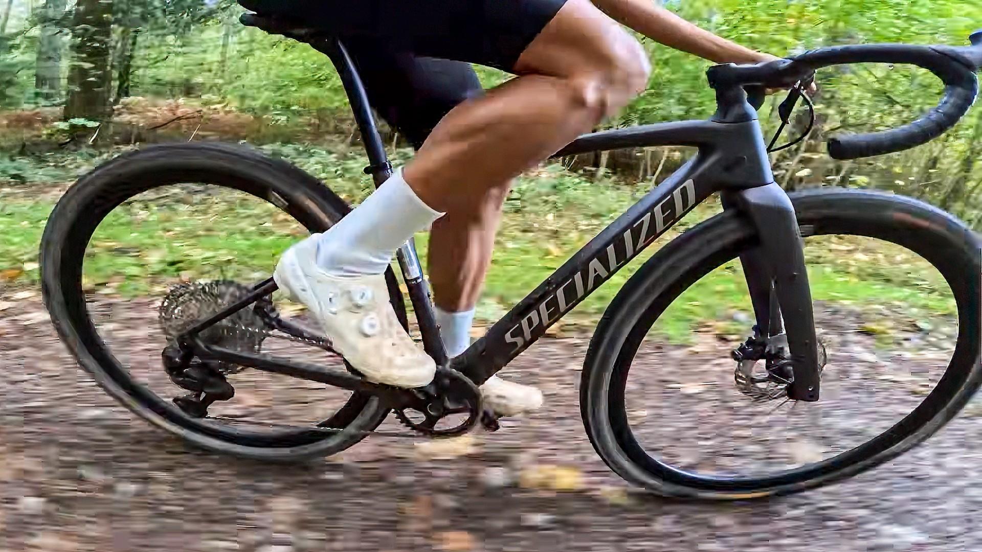 Close-up of a cyclist pedaling a Specialized road bike along a forest trail