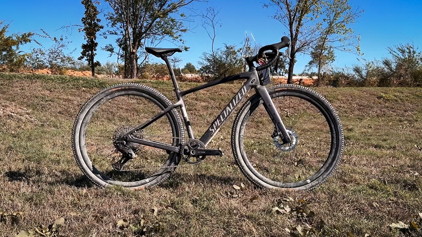 A black Specialized gravel bike stands on a dry grassy trail beneath a clear blue sky.