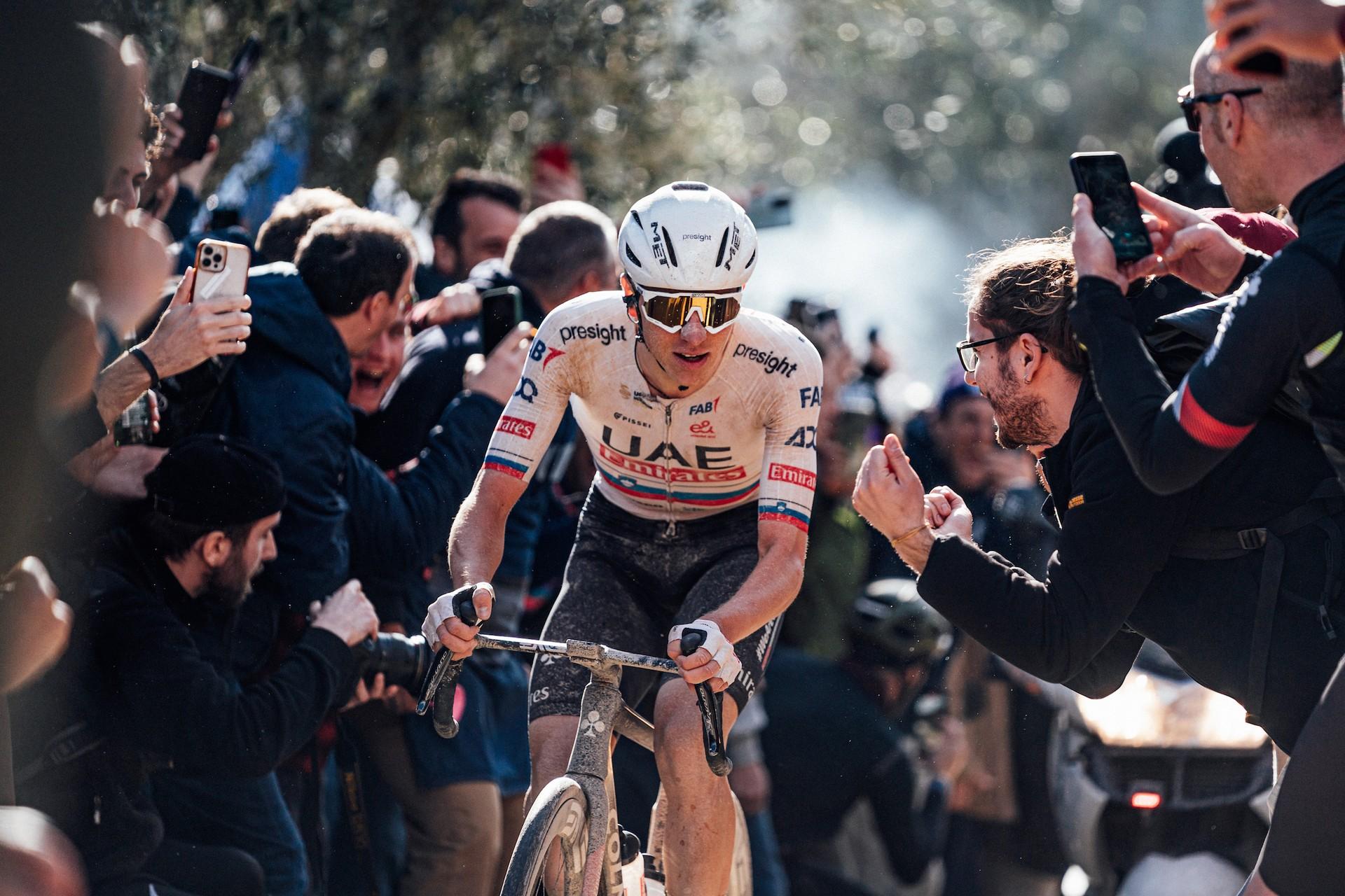 Tadej Pogačar of UAE Team Emirates rides through cheering crowds during the Strade Bianche gravel cycling race.