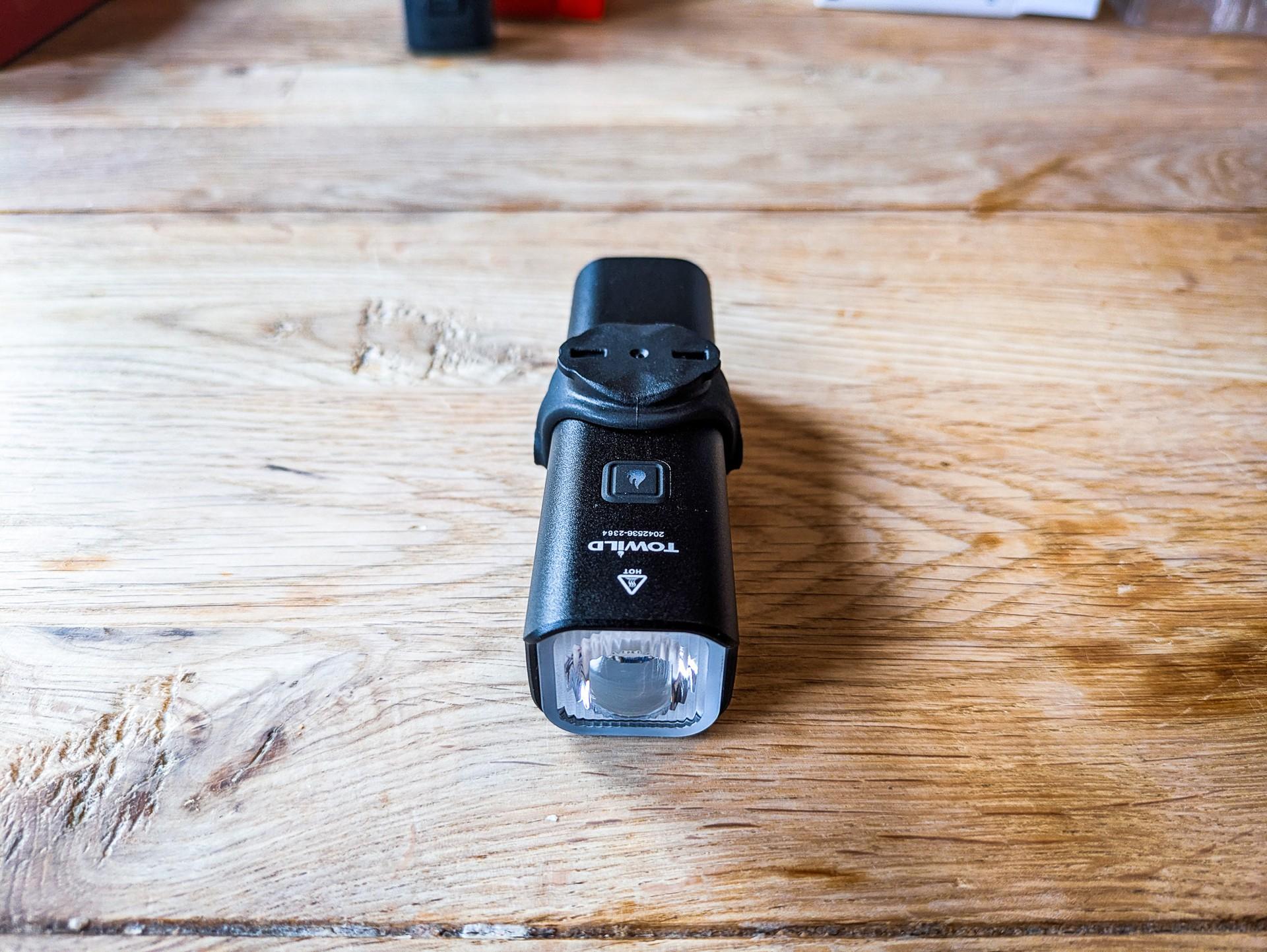 Towild CL1200 bike light standing upright on a wooden table, showing its front lens and black metal body