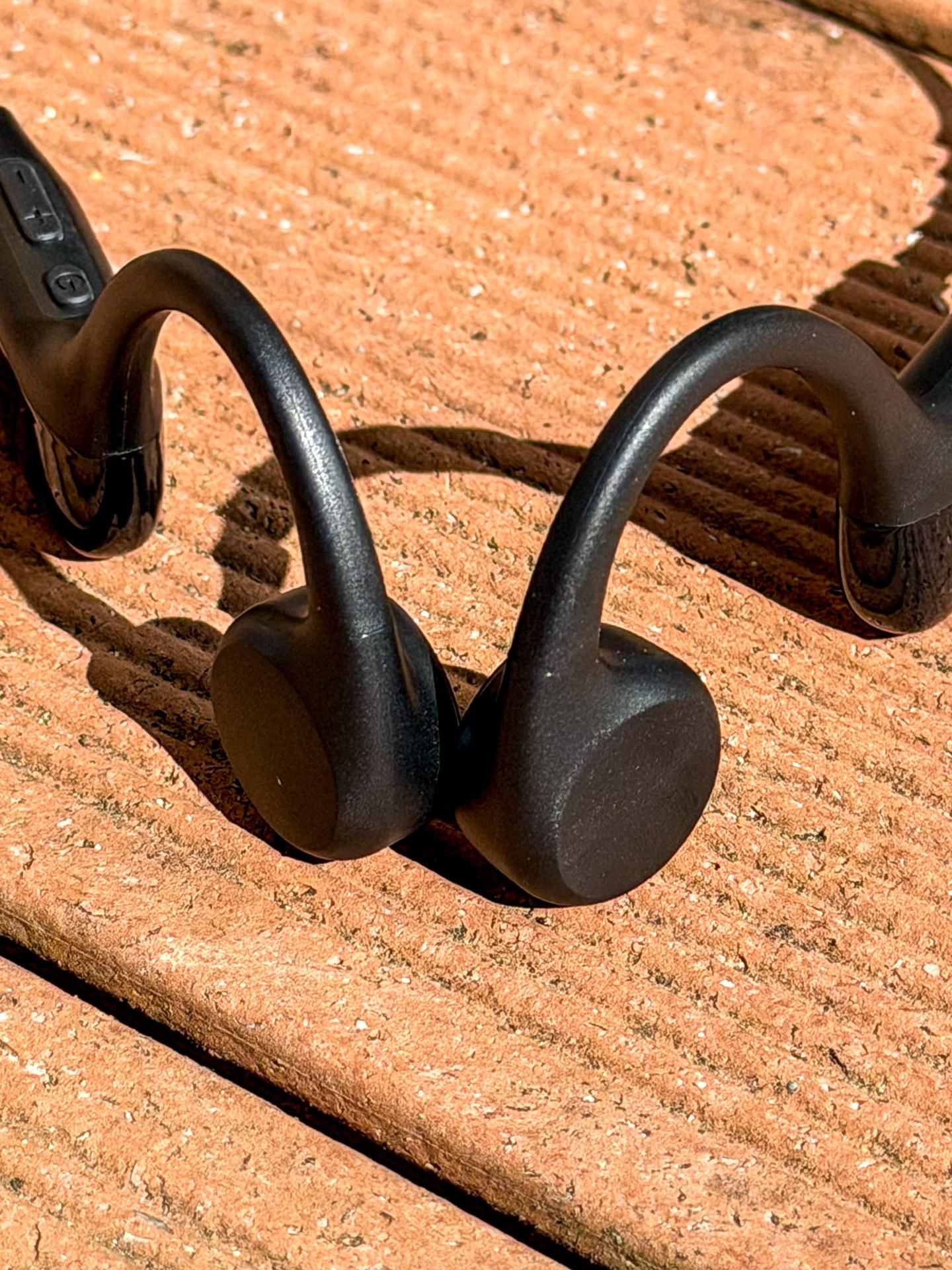 Black Zovimax bone-conduction headphones resting on a peach-colored wooden surface.