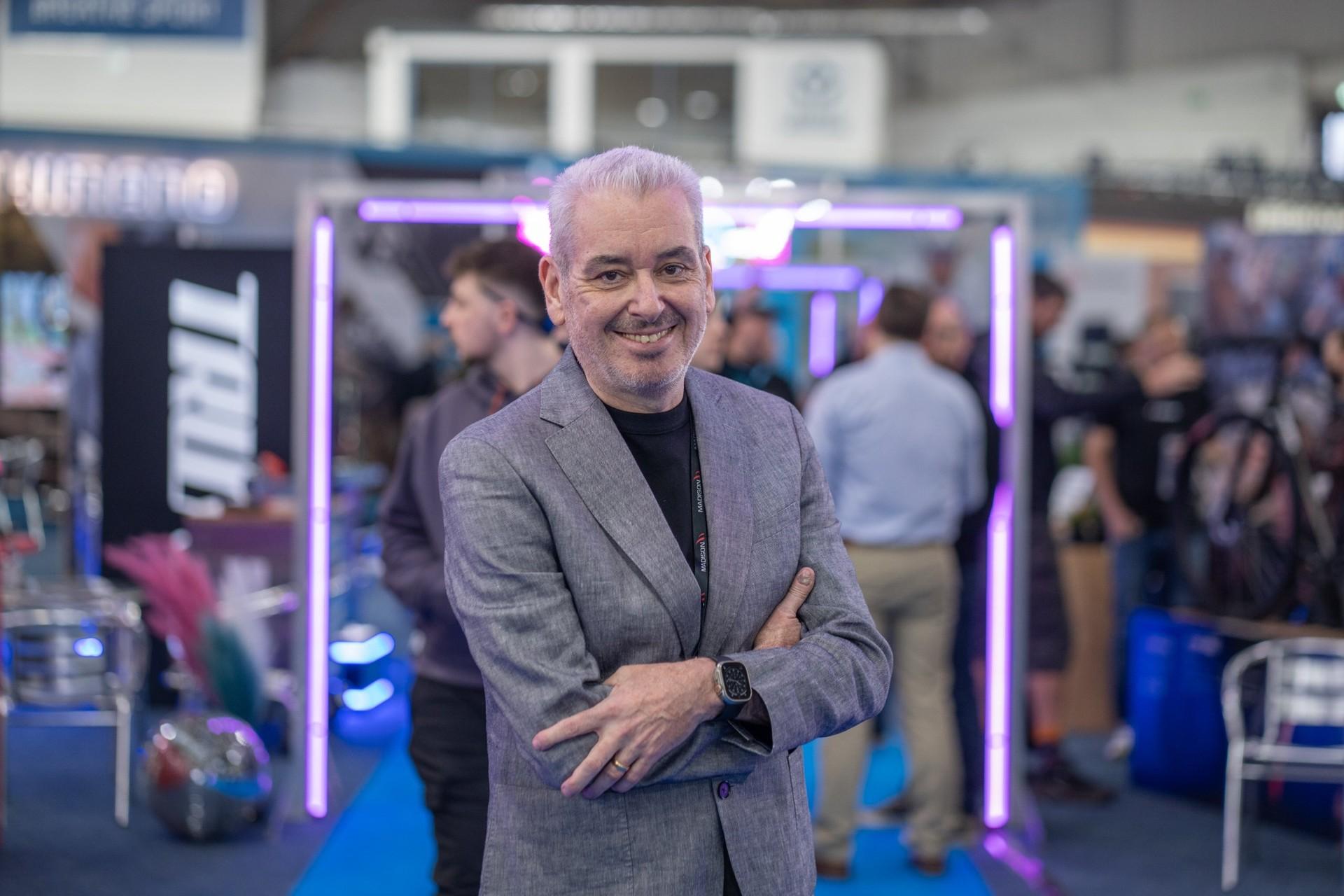 Madison CEO Dominic Langan stands with his arms crossed at the company’s trade show booth.