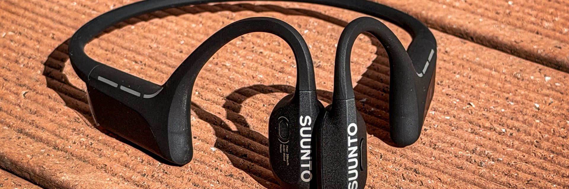 Black Suunto Wing 2 bone-conduction headphones on a wooden surface