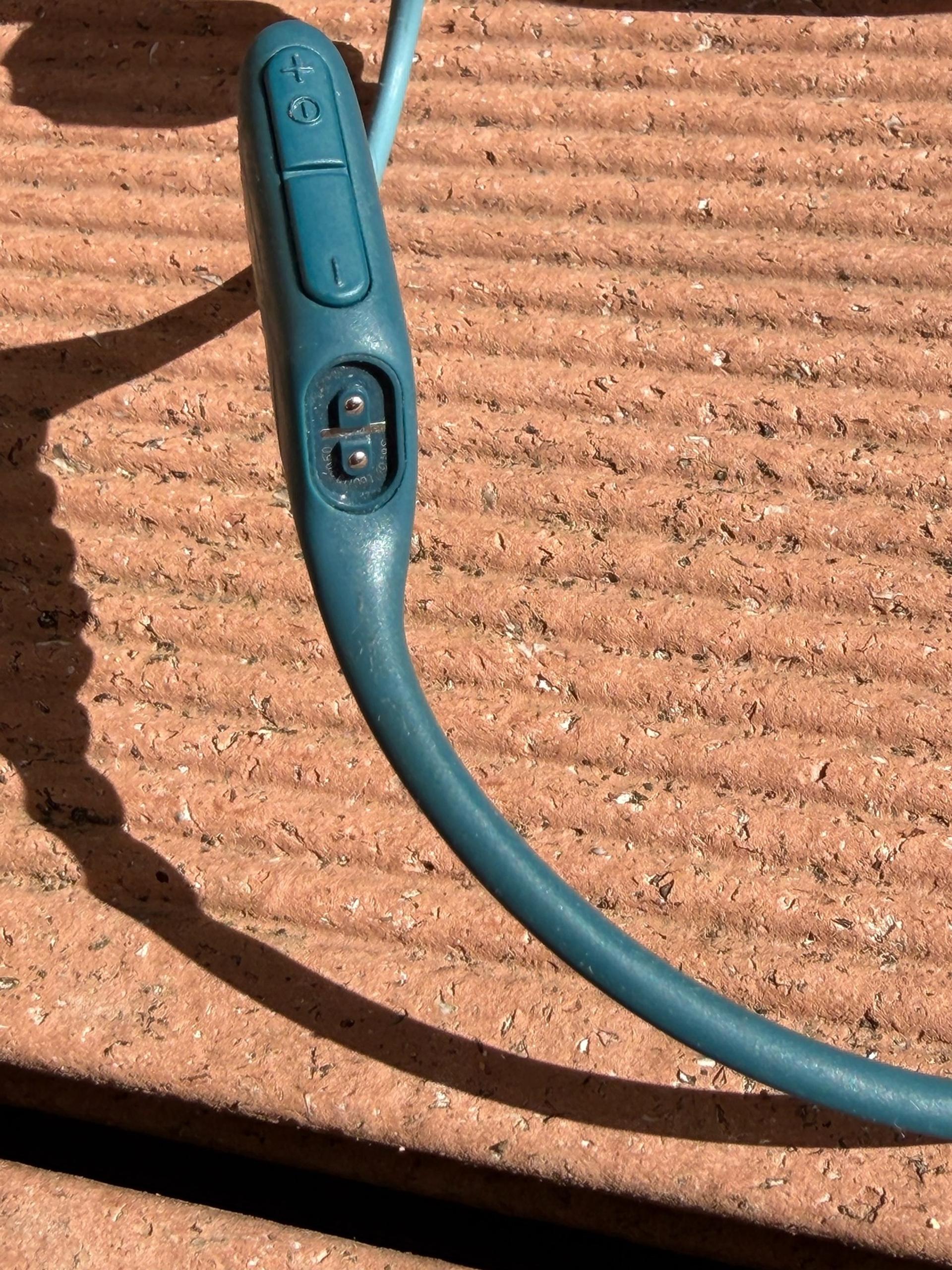 Close-up of a teal Shokz bone-conduction headset lying on a sunlit terracotta surface.