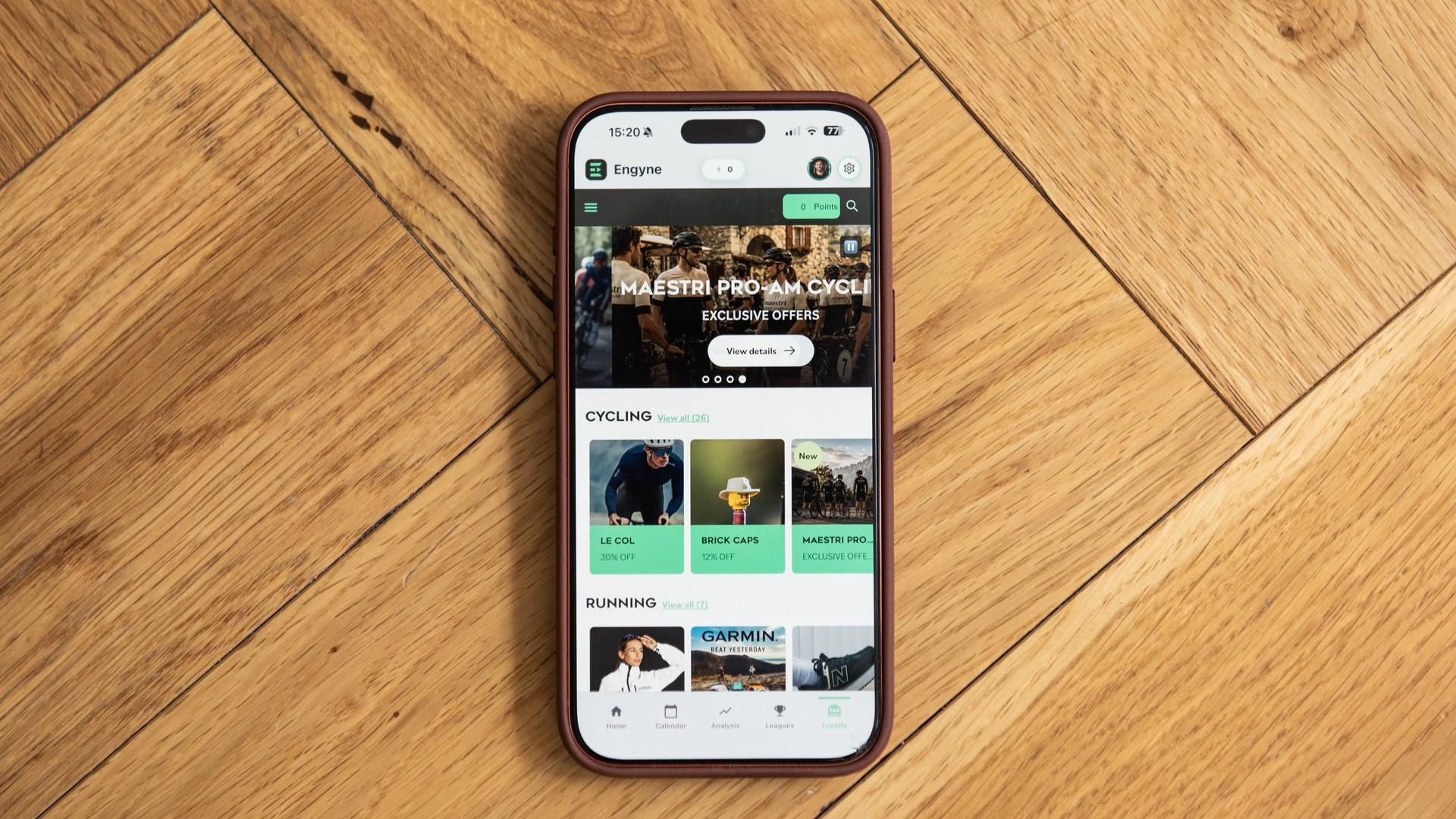 Smartphone on wooden floor showing a sports training app dashboard with cycling, running, and articles