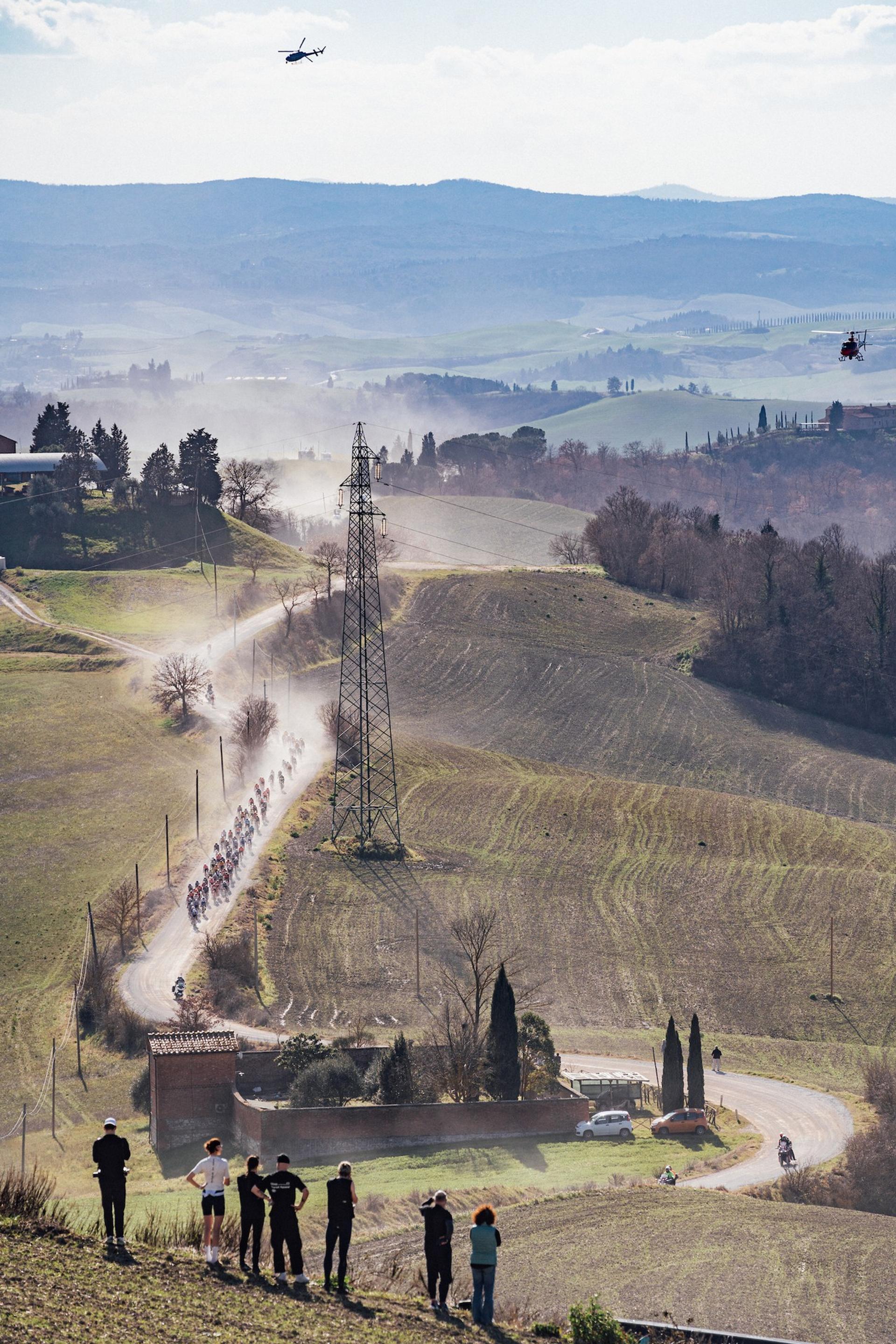 Peloton of professional cyclists racing on a dusty gravel road through the rolling Tuscan hills during Strade Bianche.