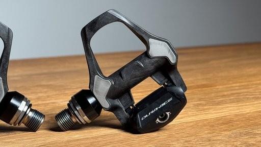 Black Shimano SPD-SLR road pedal beside another pedal on a wooden table