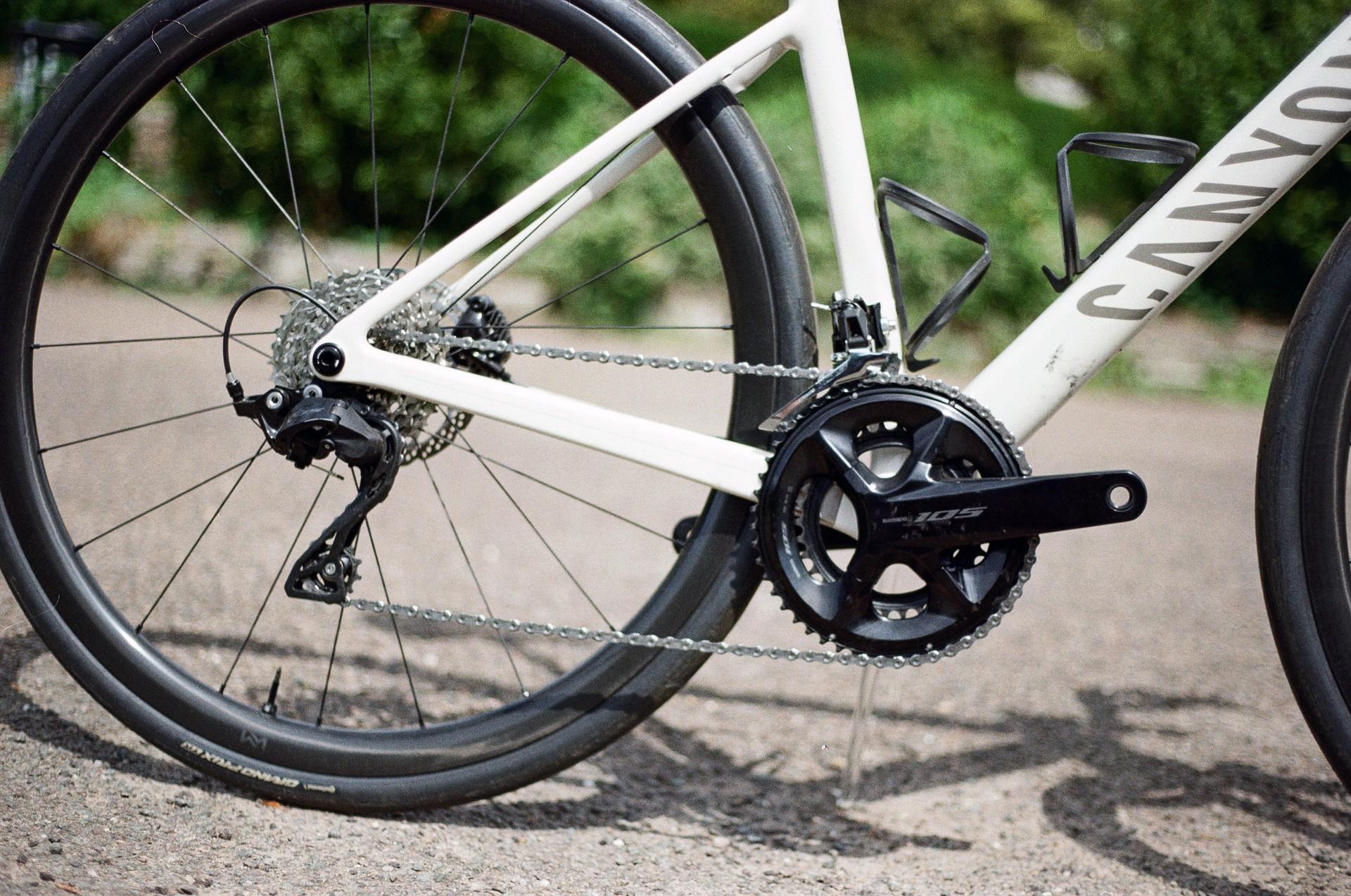 White road bike drivetrain and rear derailleur on a sunlit paved path