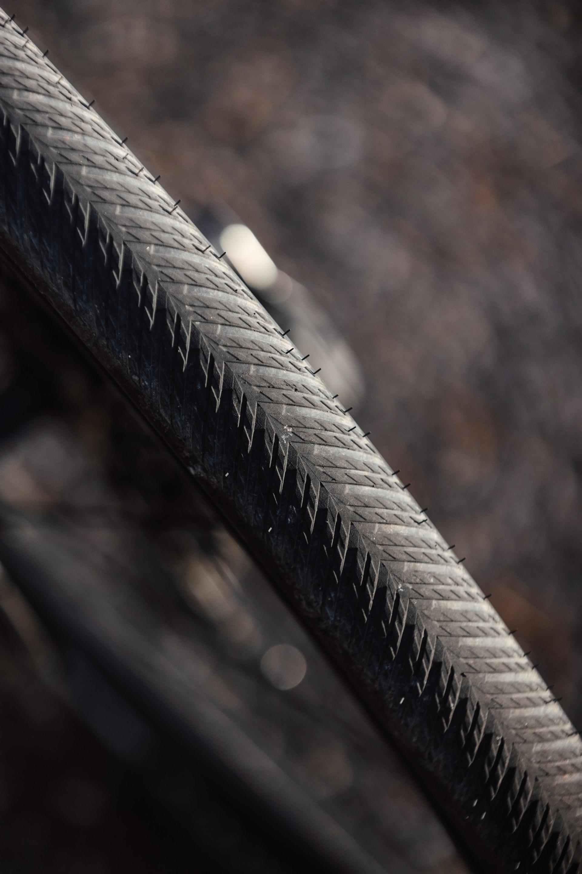 Close-up of a bicycle tire featuring a herringbone tread pattern against a blurred dark background.