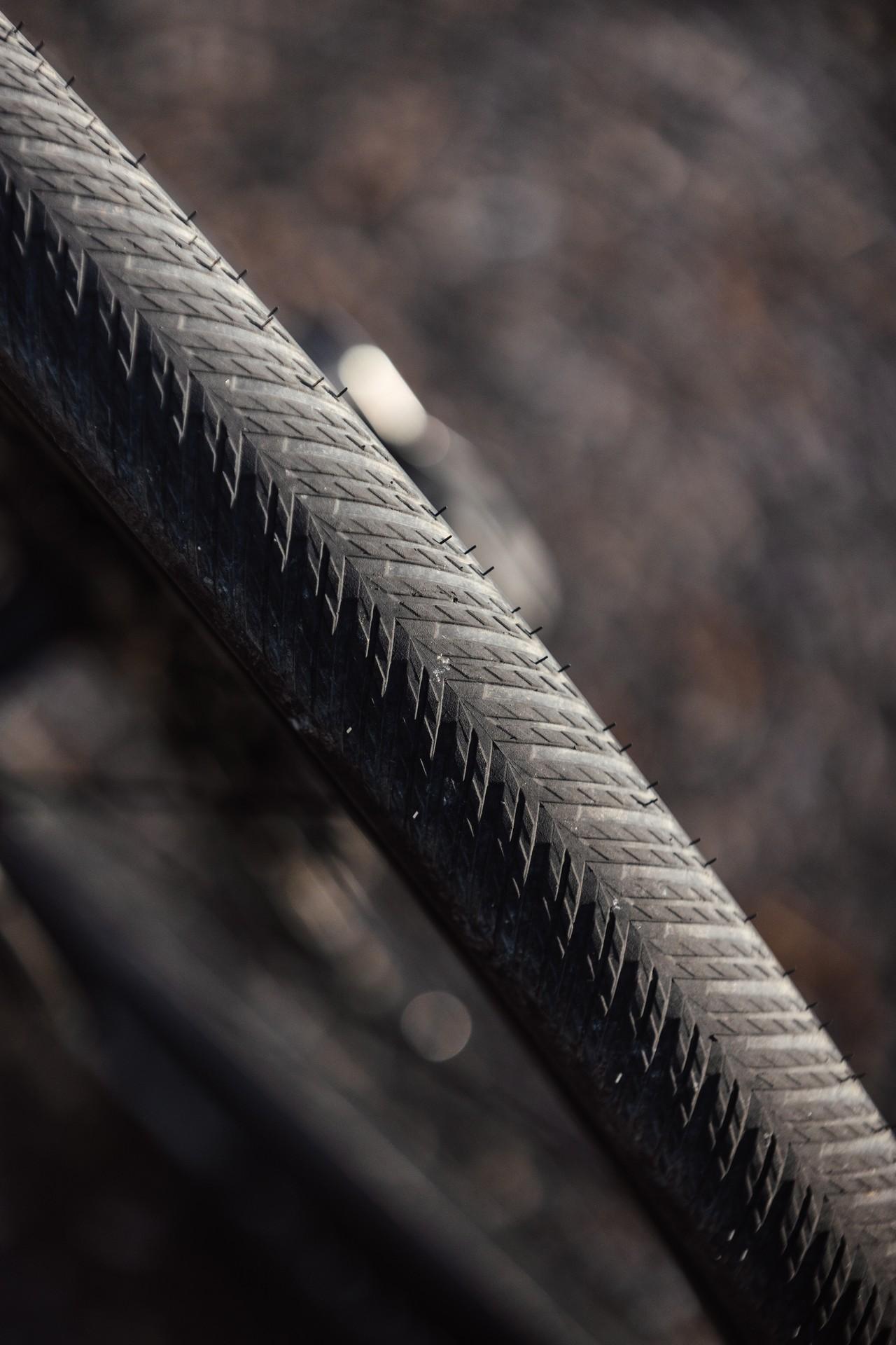 Close-up of a bicycle tire featuring a herringbone tread pattern against a blurred dark background.