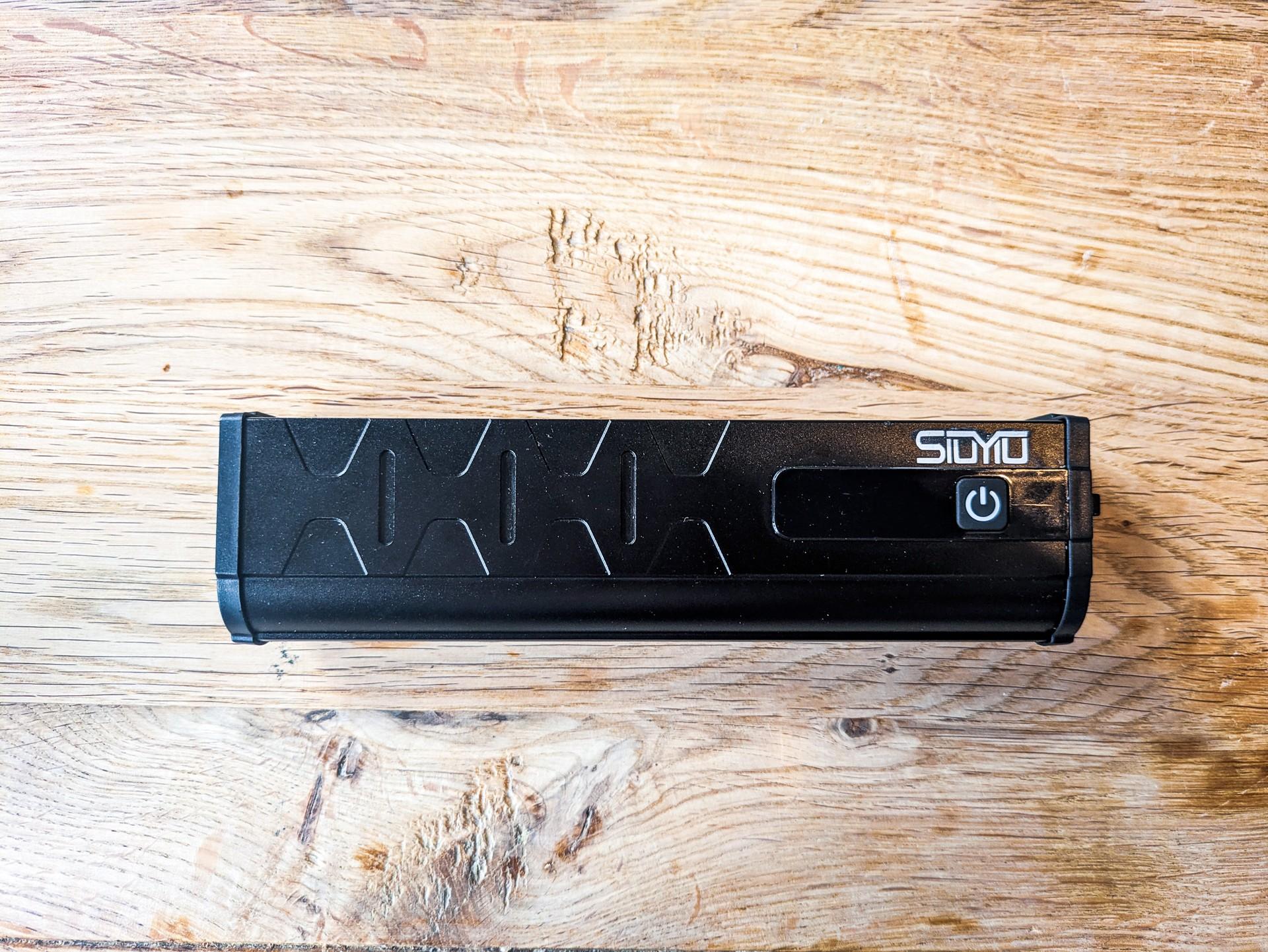 Sioyio W617 front bike light on a wooden surface, showing its wide black housing and power button