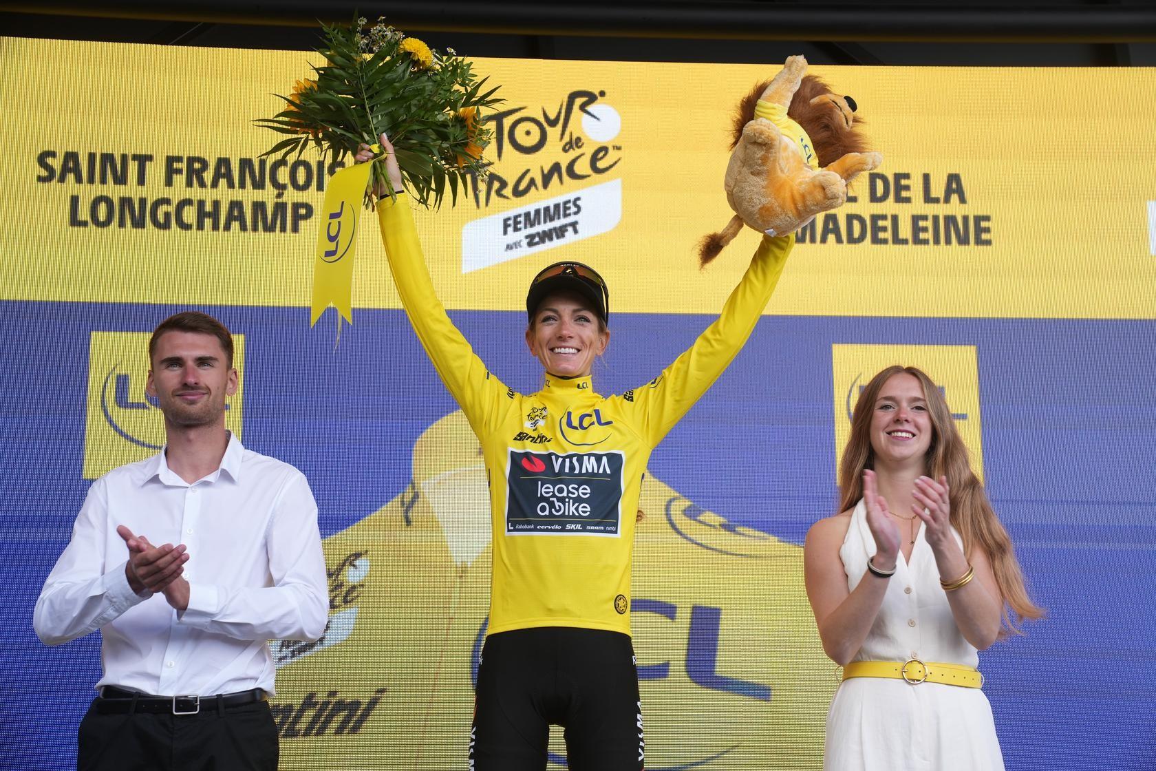 Cyclist in yellow jersey and winner’s pose on the Tour de France podium, holding both arms up