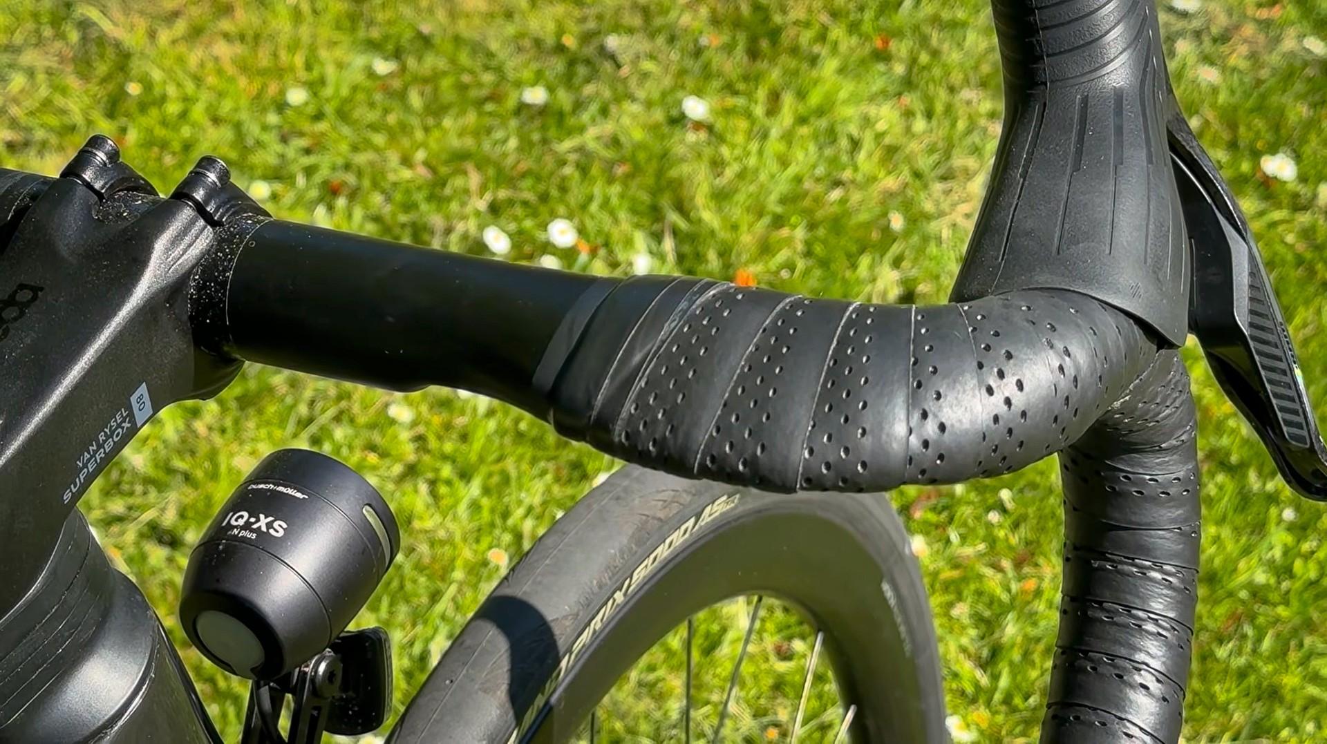 Close-up of a road cyclist’s handlebars and bar tape during a race on grass
