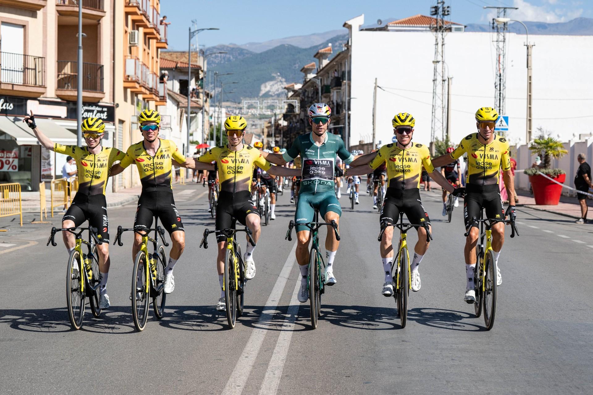 Wout van Aert rides in the green points jersey alongside five teammates through a Spanish town, with mountains behind