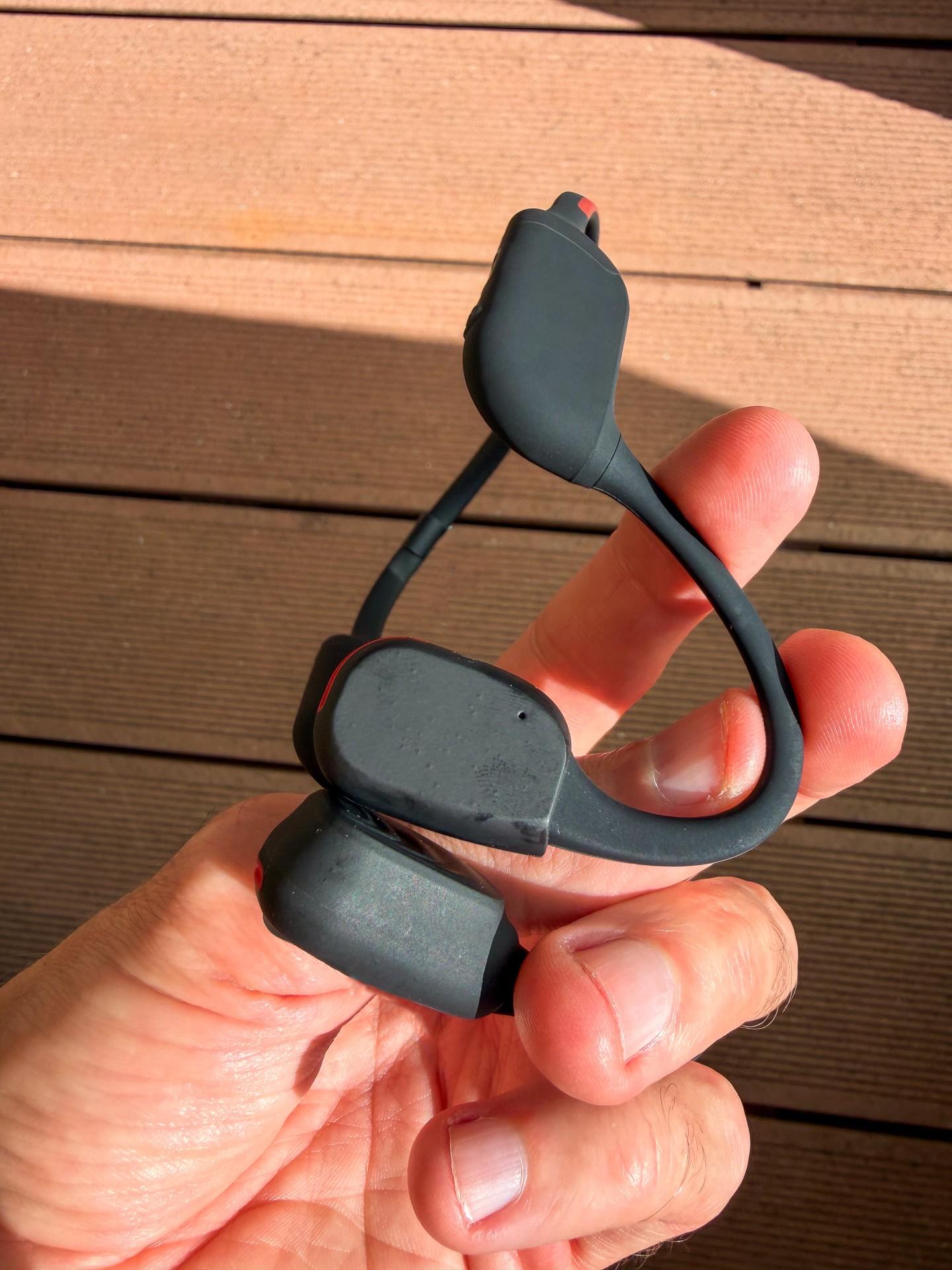 A hand holds the Philips open-ear sports headphones, showing the neckband and earpieces.