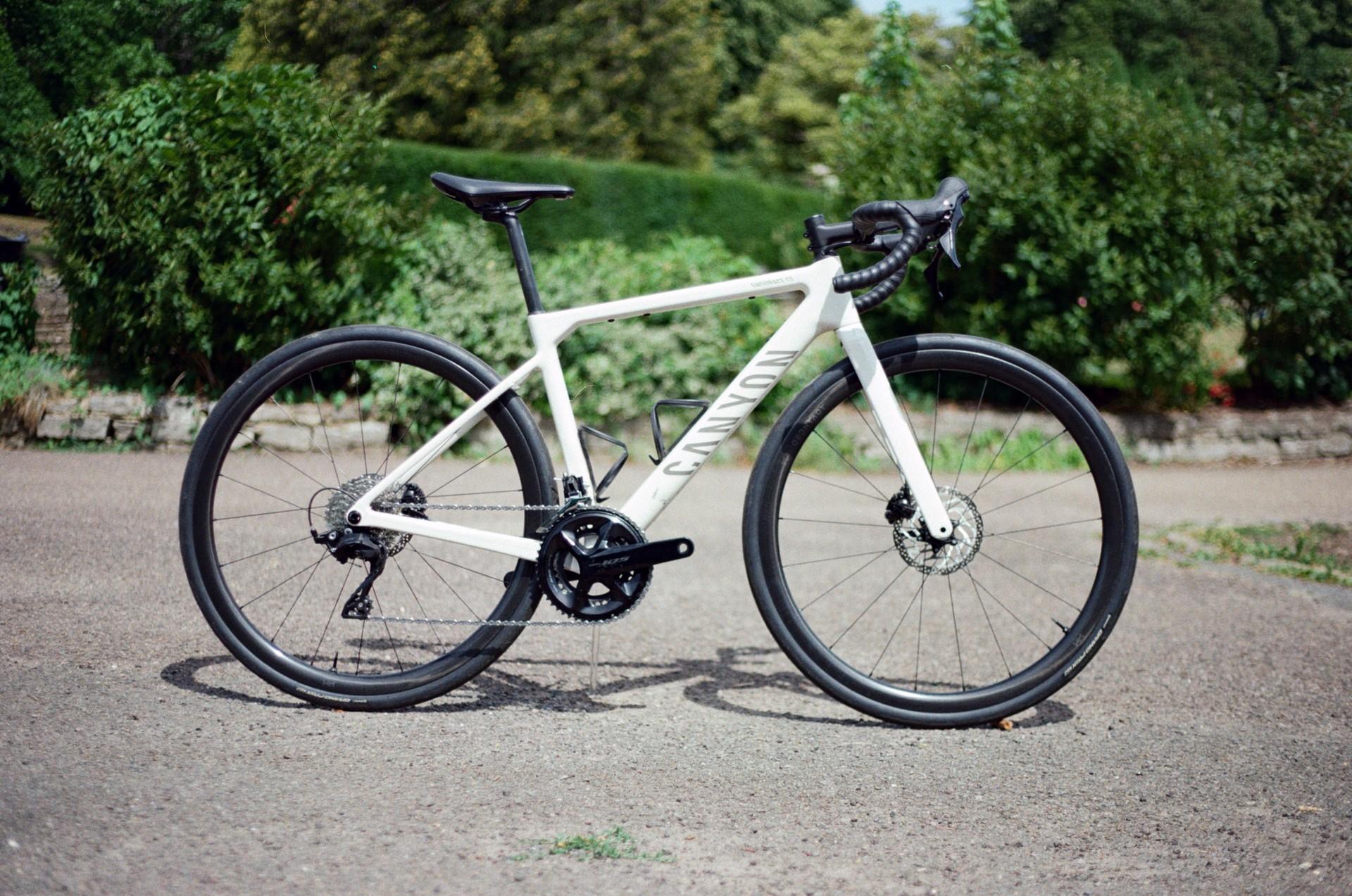 White road bike standing outdoors on a paved road with trees and greenery in the background