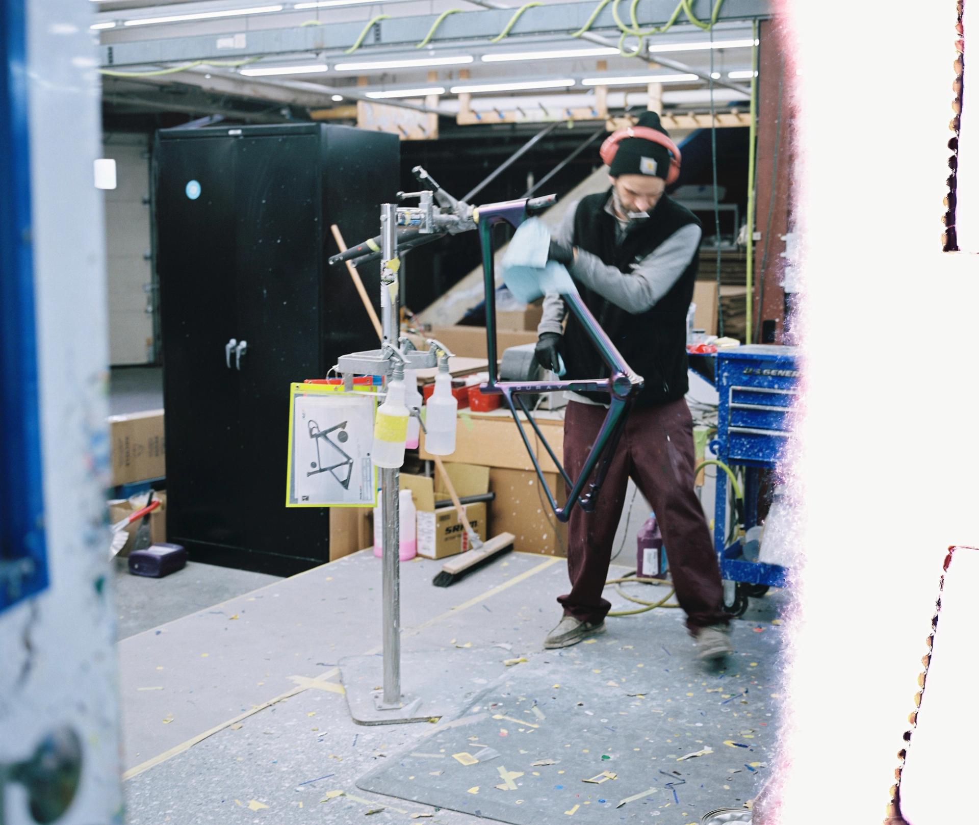 A worker in protective gear operates spray equipment inside Parlee's paint booth, mist catching the light as they coat a bicycle frame.