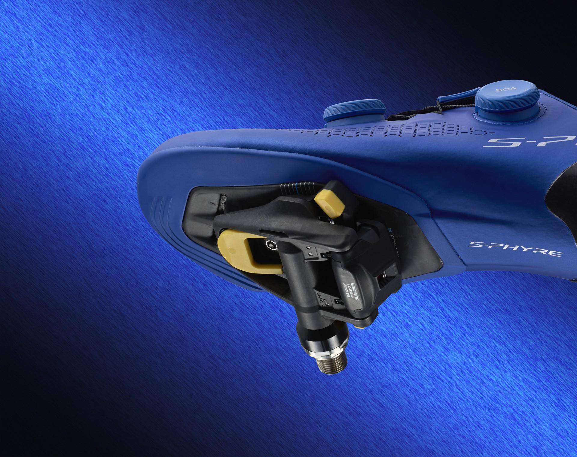Close-up of a blue Shimano S-Phyre cycling shoe fitted with an SPD-SLR pedal and yellow cleat
