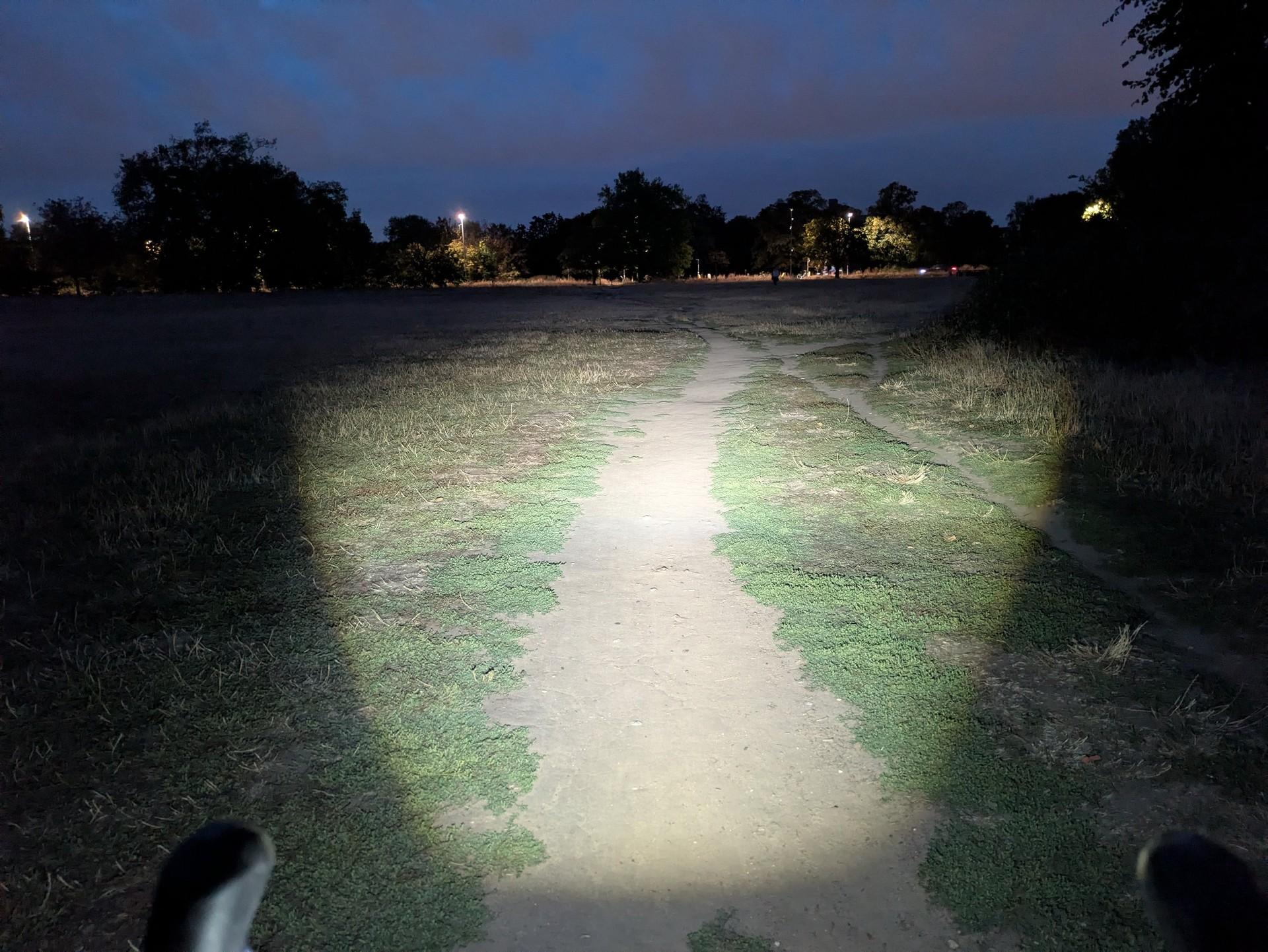 A Magicshine HORI 1300 bike light illuminates a dirt path and surrounding grass at night