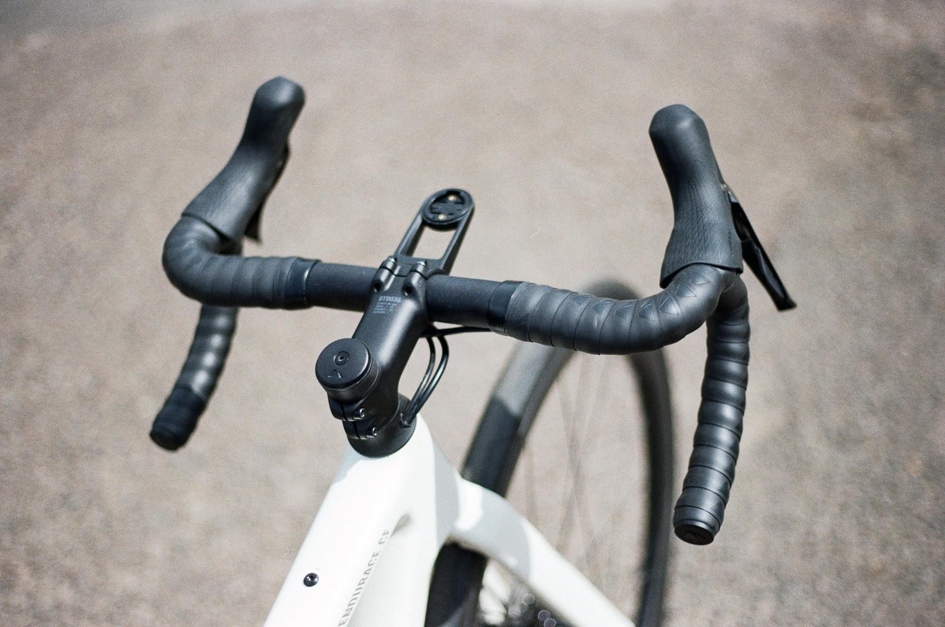 Close-up of a white road bike handlebar with dual brake hoods and mounted device on the front