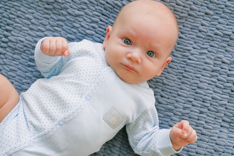 A close-up of a newborn's hand reaching out, wearing a soft, light-colored cotton sleeve.