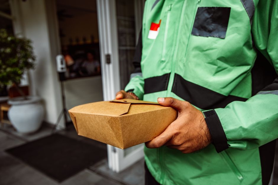 A friendly delivery person handing a package to a parent at their doorstep in Dhaka.
