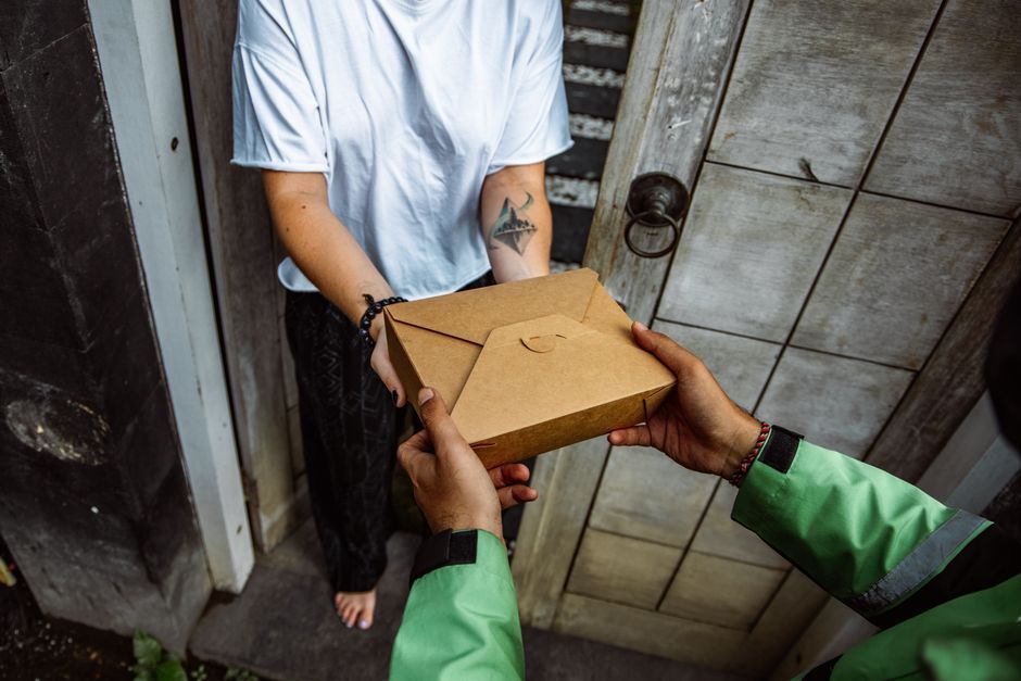 A delivery person handing a package to a parent in a bustling Dhaka neighborhood.