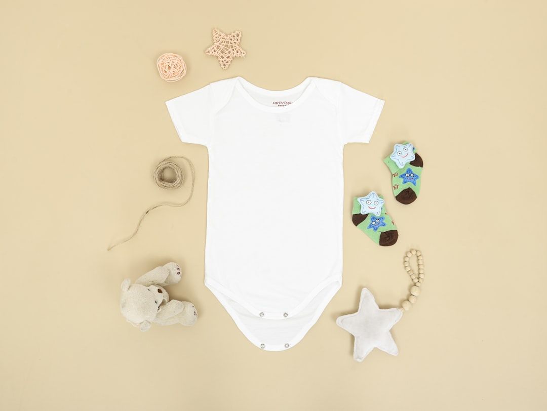 A neat stack of organic cotton baby bodysuits and sleepsuits in various pastel colors.