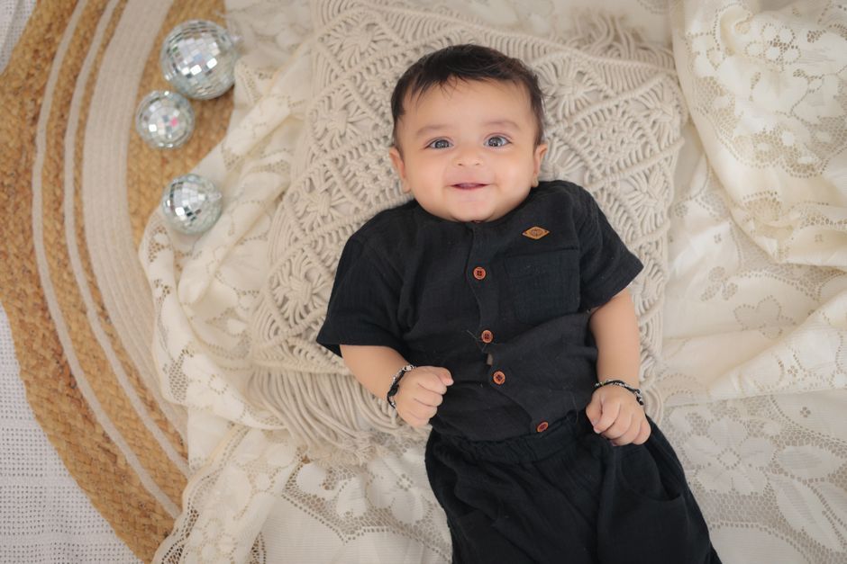 A cute baby boy dressed in a traditional Eid outfit, smiling happily.