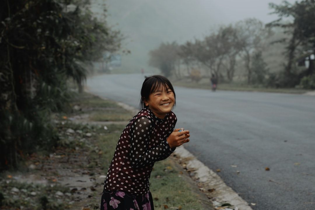 A young girl in a vibrant, flowy frock smiles as she plays in a garden with light rain falling.