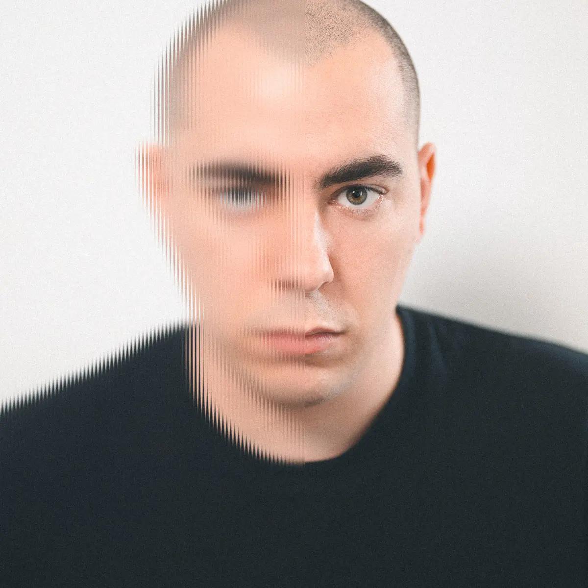 Autoportrait d'un homme au crâne rasé et au regard direct, dont le côté gauche du visage est partiellement dissimulé par l'effet strié d'un verre cannelé, créant des distorsions verticales