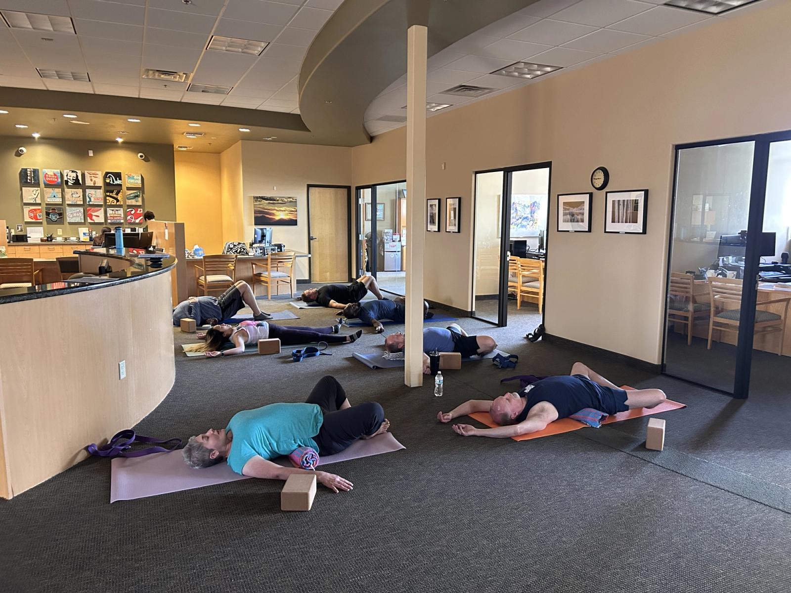 Participants resting on yoga mats in savasana during a workplace yoga session in an office.