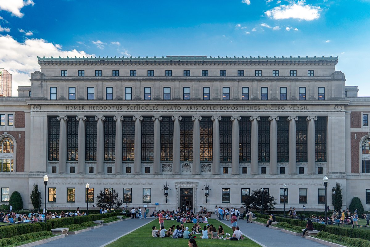 People gathered on a lawn in front of a large columned university library