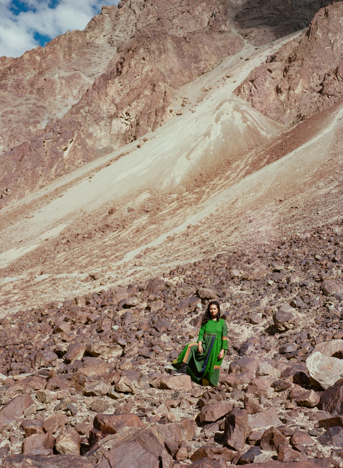 A person wearing green looking tiny against massive mountain structure with rock formations