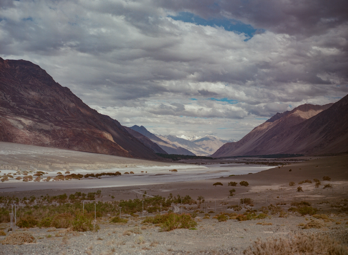 Valley in the foreground with riverbank and roads stretching out in front of mountain peaks in Sumur, Ladakh.