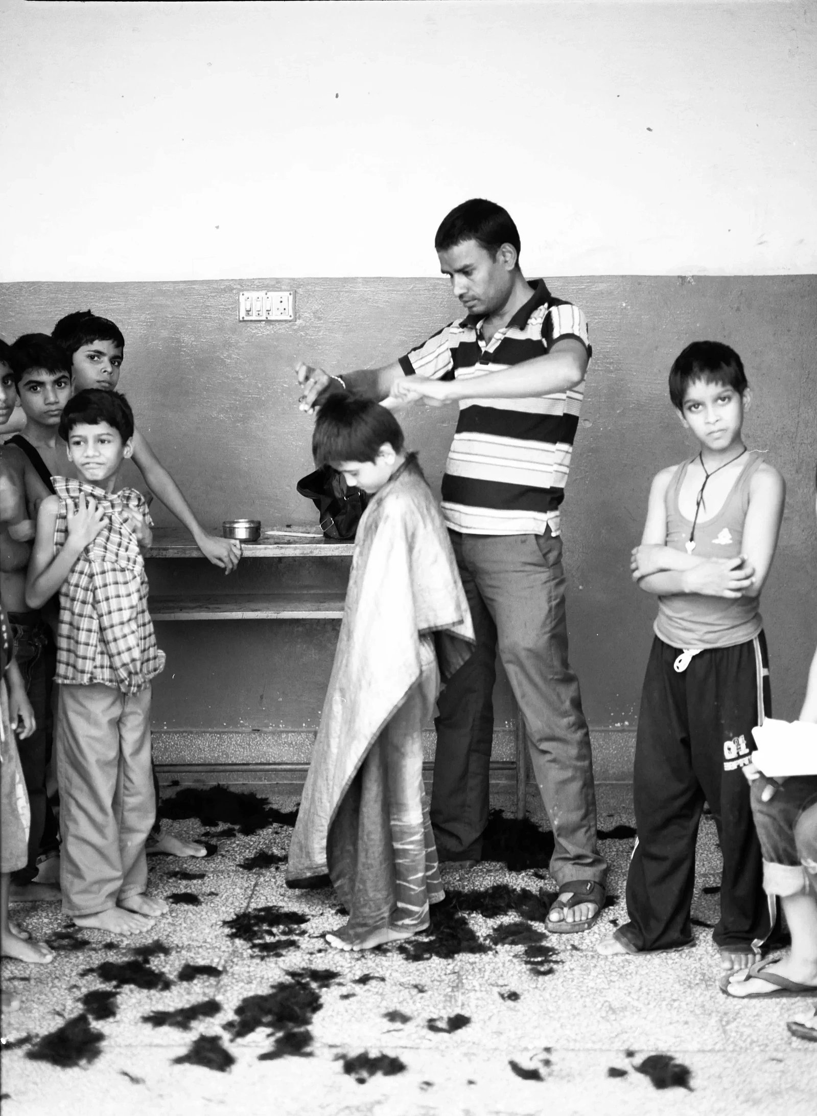 A barber cutting a child’s hair as other children look on