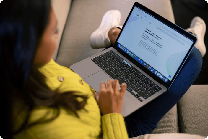 A close-up of a person sitting casually with an open laptop resting on their lap